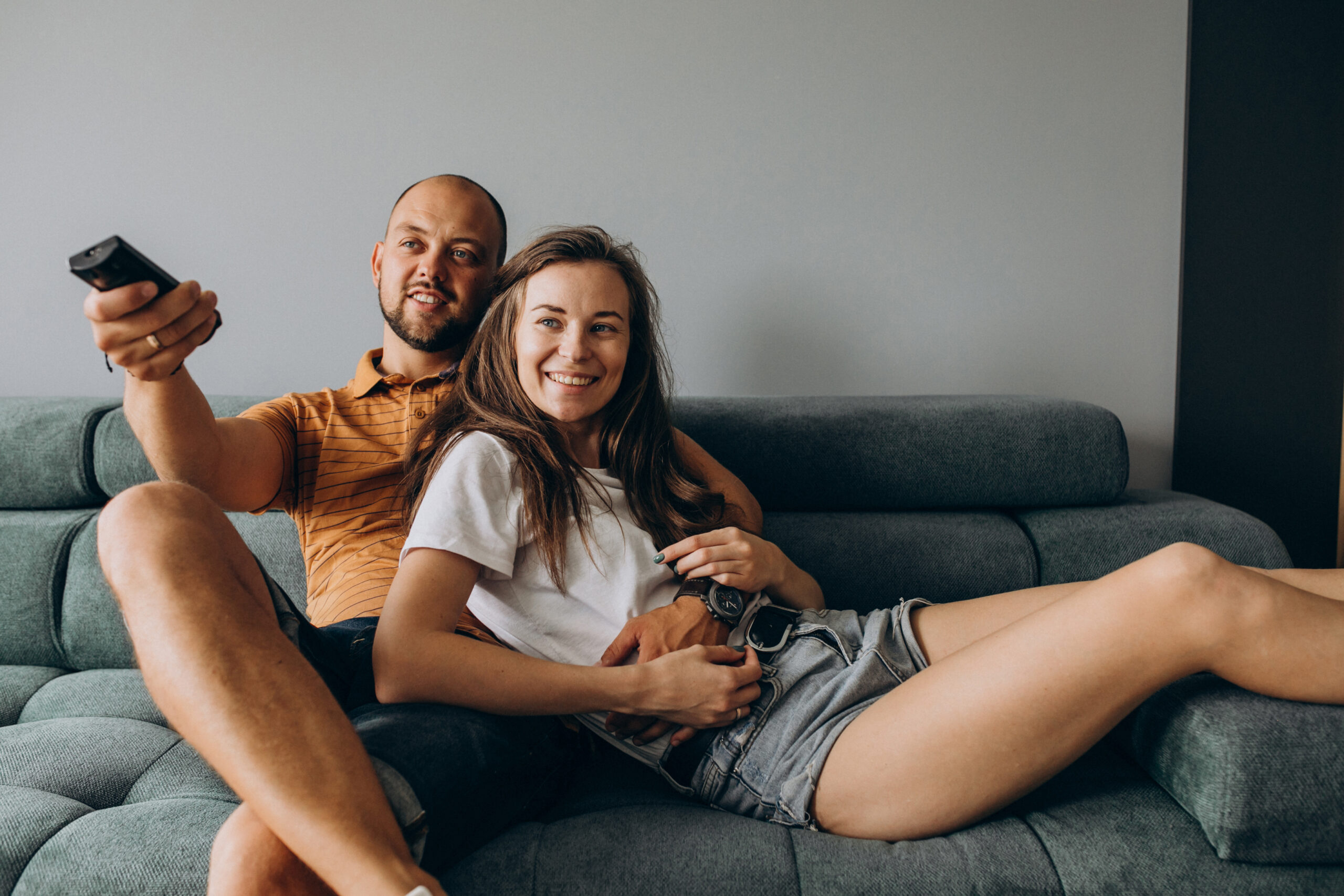 A couple watching live TV on their couch using Infinity IPTV on a smart TV in 2025